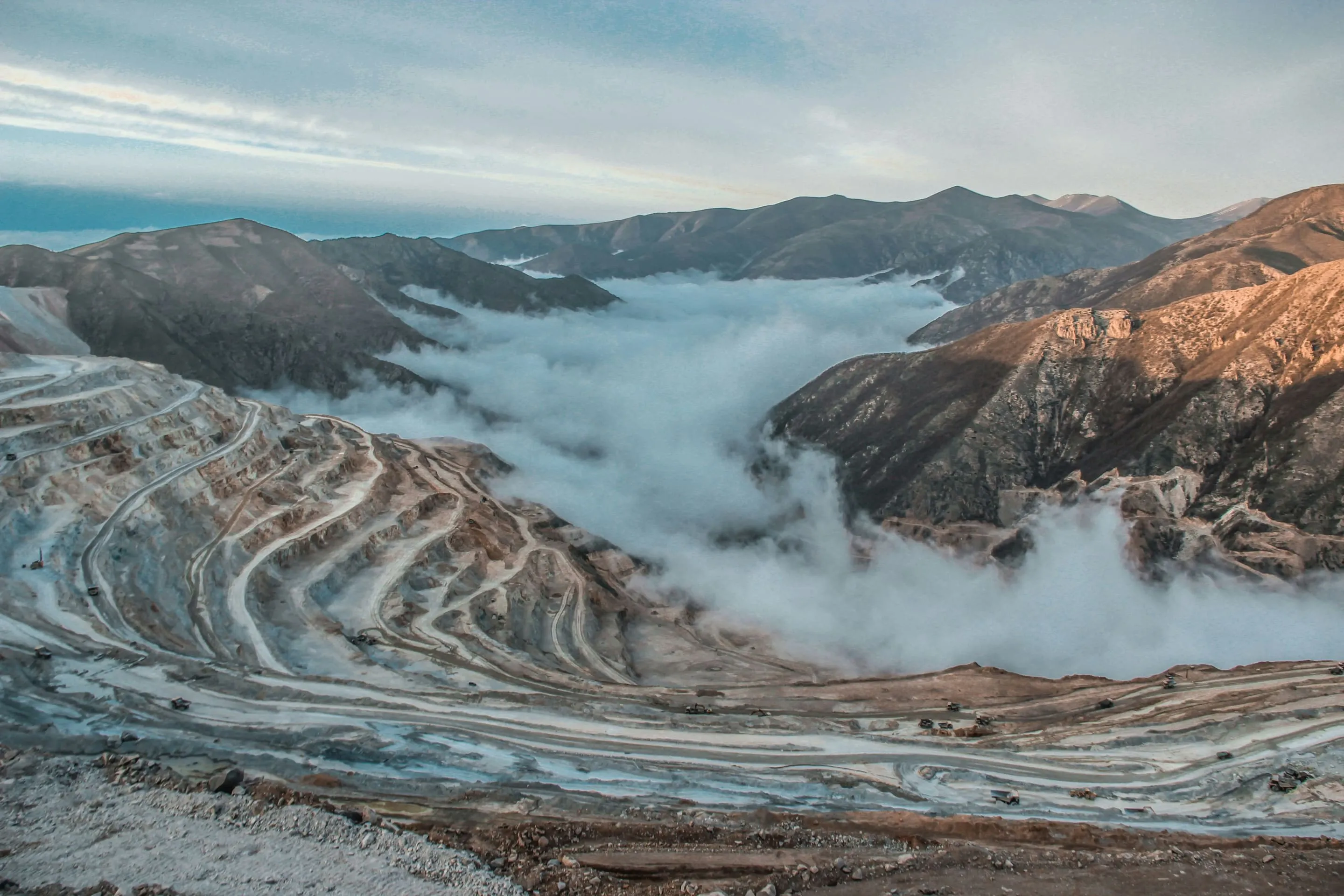 Aerial view of an open-pit mine with terraced haul roads winding between fog-covered mountains