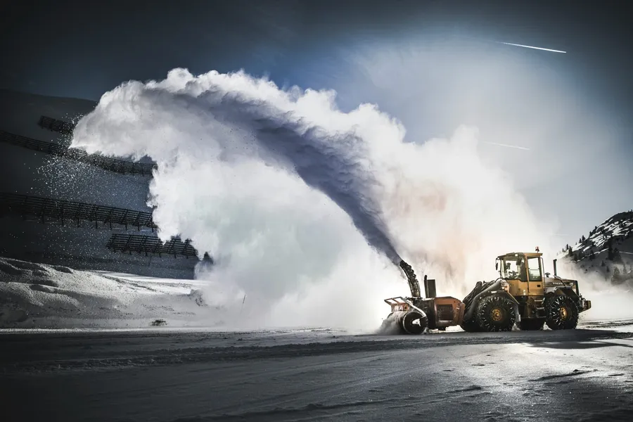 Wheel loader with a snow blower throwing a large arc of snow on an icy road
